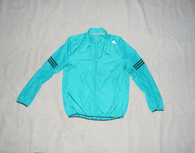 May include: A turquoise blue lightweight jacket with a zipper closure and black stripes on the sleeves.