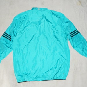 May include: A turquoise blue lightweight jacket with black stripes on the sleeves. The jacket has a zipper closure and a drawstring hood.