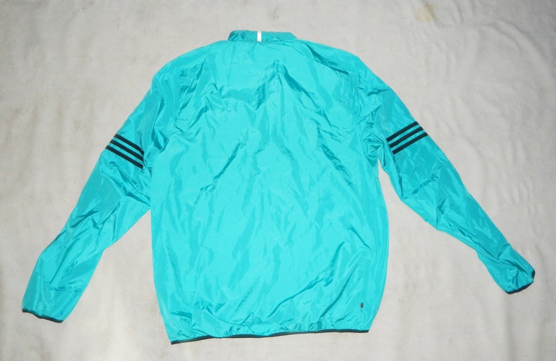 May include: A turquoise blue lightweight jacket with black stripes on the sleeves. The jacket has a zipper closure and a drawstring hood.