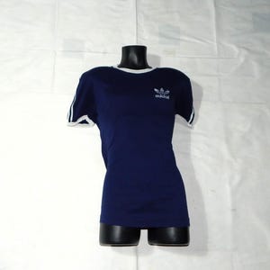 May include: A navy blue t-shirt with white trim around the neck and sleeves. The shirt has a white Adidas logo with the word "adidas" underneath.