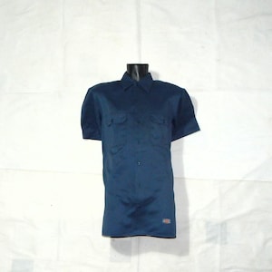 Op de afbeelding: Een marineblauw werkshirt met korte mouwen, twee borstzakken en een knoopsluiting. Het shirt heeft een klassieke kraag en een kleine logopatch bij de zoom. Gepresenteerd op een zwarte mannequin.