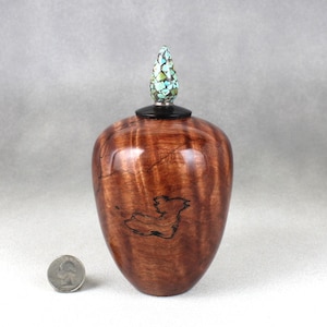 May include: A wooden vase with a unique, swirling grain pattern. The vase has a dark brown, black, and red colour scheme. The top of the vase is adorned with a decorative, multi-coloured glass stopper.