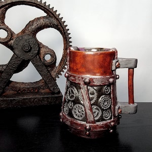Pode incluir: Uma caneca de cerâmica marrom com um design steampunk que inclui engrenagens e detalhes metálicos. A caneca tem uma alça e uma base larga.
