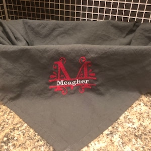 May include: Gray linen kitchen towel with a red embroidered monogram "M" and the name "Meagher" below it.