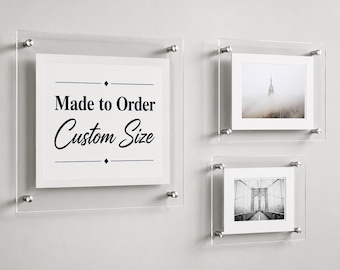 May include: Three clear acrylic floating frames with silver metal standoffs. The largest frame displays the text Made to Order Custom Size. The other two frames contain black and white photographs of a skyscraper in fog and a suspension bridge.