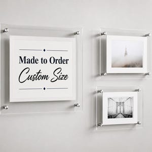 May include: Three clear acrylic floating frames with silver metal standoffs. The largest frame displays the text Made to Order Custom Size. The other two frames contain black and white photographs of a skyscraper in fog and a suspension bridge.