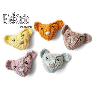 Op de afbeelding: Vijf gehaakte leeuwenkop applicaties in verschillende pastelkleuren: geel, oranje, roze, blauw en mauve. Elk heeft gesloten ogen en een kleine neus. De tekst "BieKado Pattern" staat in de linkerbovenhoek.