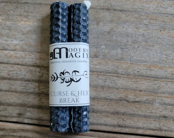 May include: Two black beeswax candles with a honeycomb pattern. The label reads "Modern Magix" and "Beeswax Intention Candles" with a graphic of an arrow and the text "Curse & Hex Break".