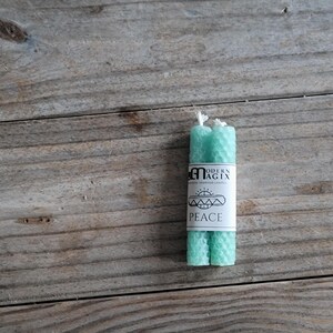 May include: Two teal green beeswax candles with a label that reads "Modern Magix" and "Peace".