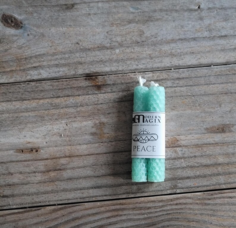 May include: Two teal green beeswax candles with a label that reads "Modern Magix" and "Peace".