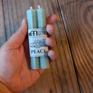 May include: Two blue beeswax candles with a label that reads "Modern Magix beeswax intention candles" and "Peace".
