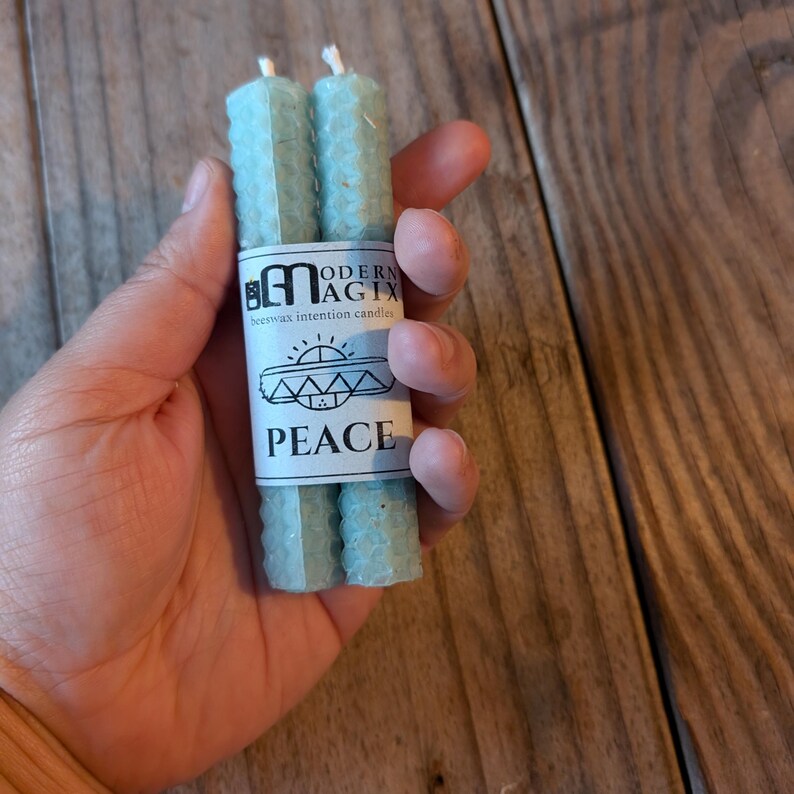 May include: Two blue beeswax candles with a label that reads "Modern Magix beeswax intention candles" and "Peace".