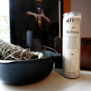 May include: A white soy candle with the text "Modern Agix" and "Beltane" printed on the label. The candle is decorated with a geometric design and the text "Spring Bonfire".