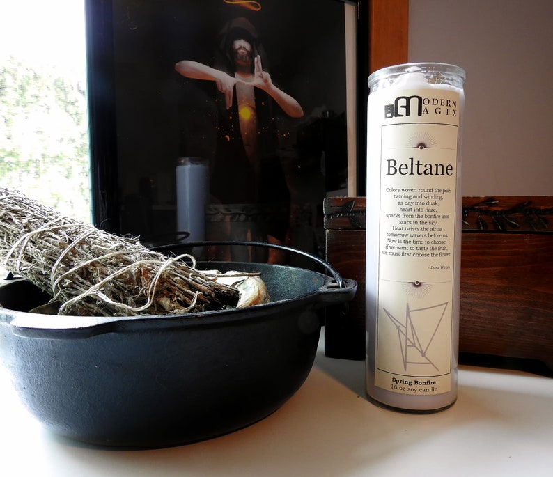 May include: A white soy candle with the text "Modern Agix" and "Beltane" printed on the label. The candle is decorated with a geometric design and the text "Spring Bonfire".