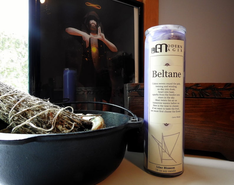 May include: Purple soy candle with a white label that reads "Modern Agix Beltane" and includes a description of the holiday. The candle is 18 oz and has a lilac blossom scent.
