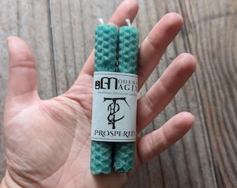 May include: Two green beeswax candles with a honeycomb texture. The candles are labeled "Modern Magix" and "Prosperity".