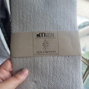 May include: A white, textured, handmade paper sheet with a brown label that reads "Modern Agix, herb infused intention paper, Quick Results, hand-crafted from recycled material."