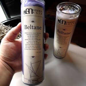 May include: Two purple and white candles with the text "Beltane" and a poem about the holiday. The candles are labeled "Modern Agix" and are 16 oz soy candles.