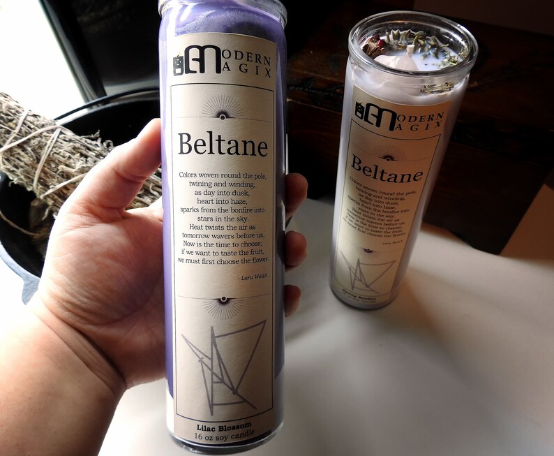 May include: Two purple and white candles with the text "Beltane" and a poem about the holiday. The candles are labeled "Modern Agix" and are 16 oz soy candles.