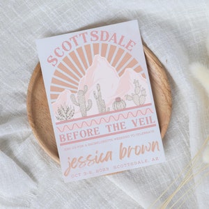 May include: A pink and white illustrated invitation for a bachelorette party in Scottsdale, Arizona. The invitation features a desert landscape with mountains, cacti, and a sunset. The text reads "Scottsdale Before the Veil Join us for a bachelorette weekend to celebrate Jessica Brown Oct 3-5, 2023 Scottsdale, AZ"