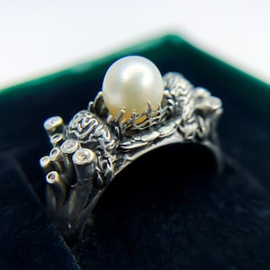 May include: A silver ring with a pearl and small diamonds set in a detailed design resembling coral and sea life.
