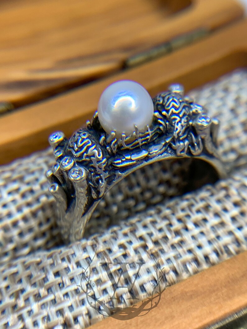 May include: A silver ring with a pearl set in a detailed design of branches and leaves.