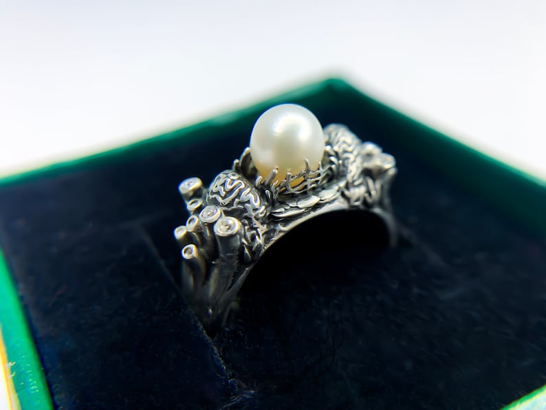 May include: A silver ring with a pearl and small diamonds set in a detailed design resembling coral and sea life.