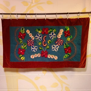 May include: A red velvet wall hanging with a blue embroidered floral design. The flowers are in shades of red, pink, yellow, and white.
