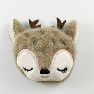 May include: A brown plush deer with closed eyes and embroidered details. The deer has a small black nose and pink cheeks.