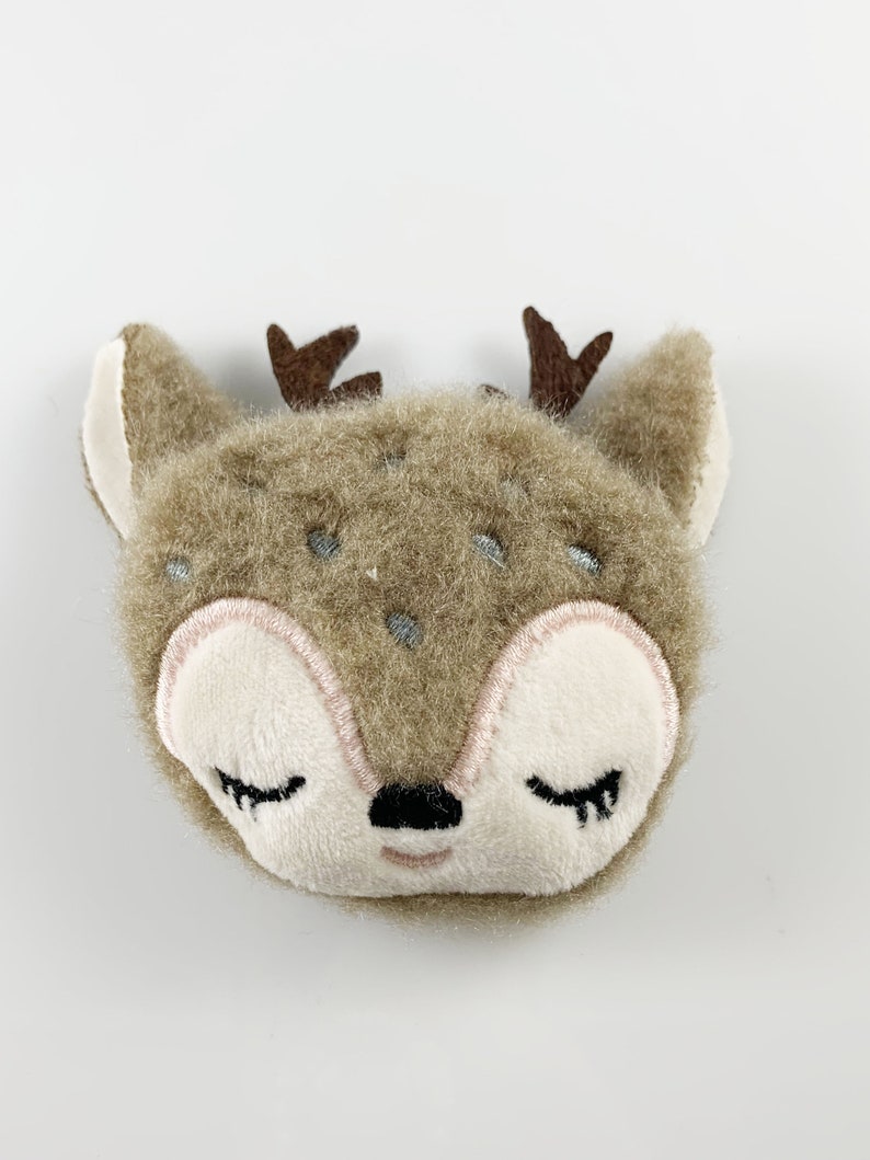 May include: A brown plush deer with closed eyes and embroidered details. The deer has a small black nose and pink cheeks.