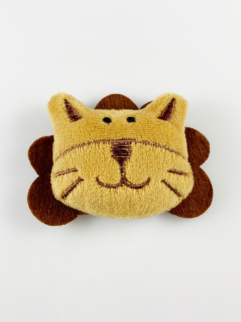 May include: A plush lion head toy with brown ears and a brown mane. The lion has a stitched-on face with brown eyes, a nose, and whiskers.