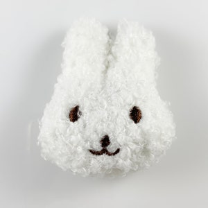 May include: White fluffy bunny plush toy with brown embroidered eyes and a smiling mouth.