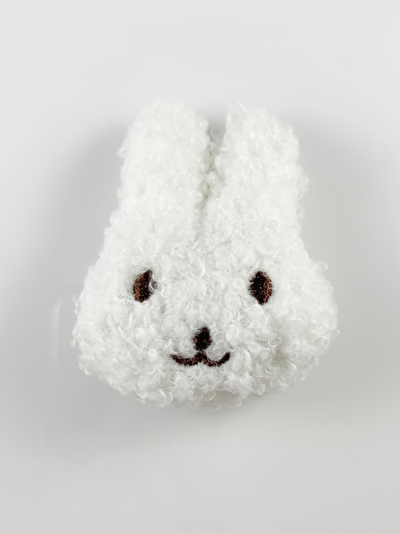 May include: White fluffy bunny plush toy with brown embroidered eyes and a smiling mouth.
