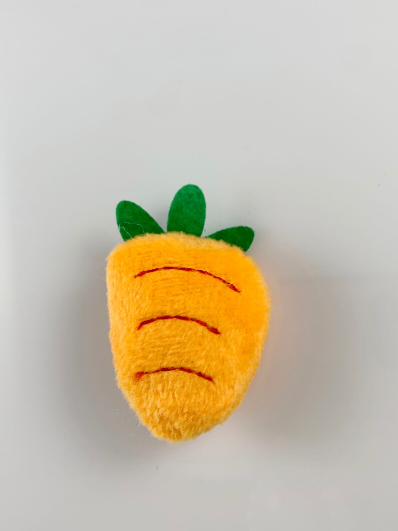 May include: A plush orange carrot toy with green leaves. The carrot has embroidered lines to resemble the ridges of a real carrot.