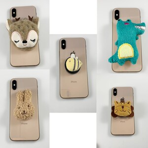 May include: Five different phone cases with cute animal and insect designs. The cases are all gold and have the word "iPhone" printed on the back. The designs include a deer, a bee, a crocodile, a bunny, and a lion.
