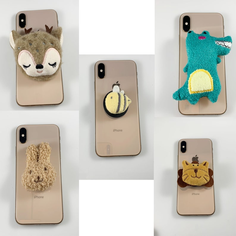 May include: Five different phone cases with cute animal and insect designs. The cases are all gold and have the word "iPhone" printed on the back. The designs include a deer, a bee, a crocodile, a bunny, and a lion.