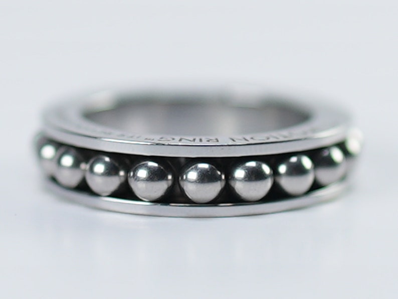 Puede incluir: Un anillo de plata con una fila de peque&ntilde;as cuentas de plata alrededor de la banda. El anillo est&aacute; inscrito con las palabras "NORM RING".