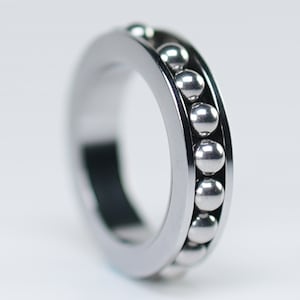 May include: A silver metal ring with a row of small silver balls around the outside.