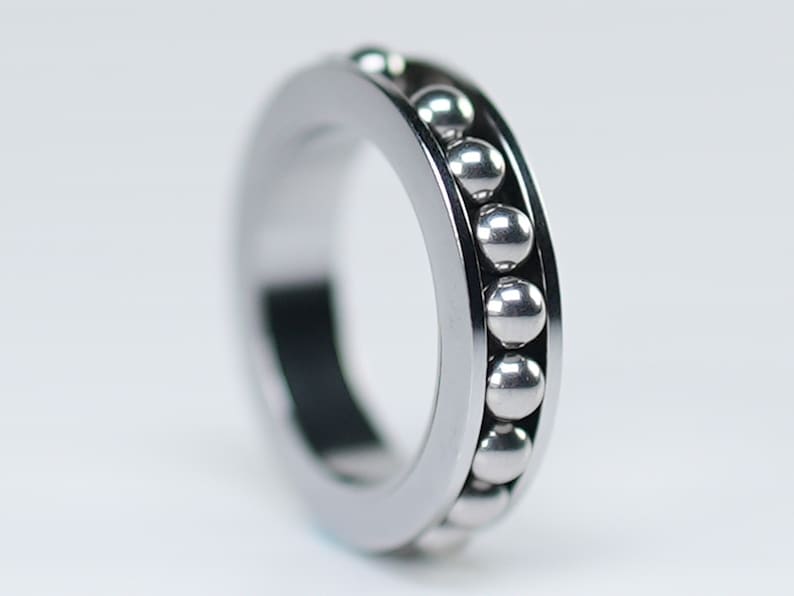 Puede incluir: Un anillo de metal plateado con una fila de peque&ntilde;as bolas plateadas alrededor del exterior.