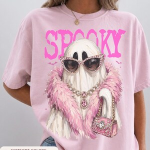 A pink t-shirt with a graphic design of a ghost wearing sunglasses, a pink fur coat, and a pink purse.