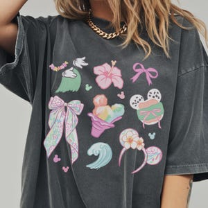 A person wearing a gray t-shirt with various Disney-themed illustrations, including Mickey Mouse, flowers, and other whimsical designs.