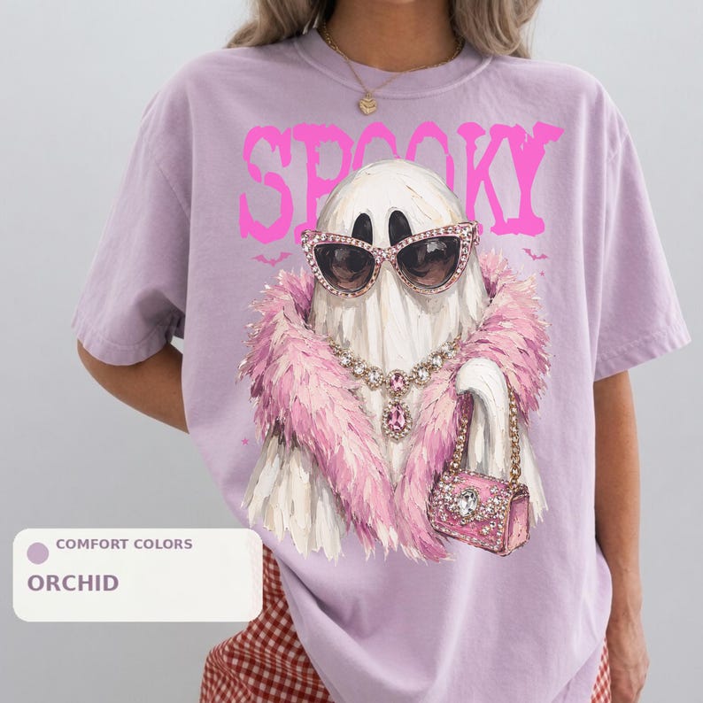 A person wearing a purple t-shirt with a graphic design of a ghost wearing sunglasses, a pink feathered scarf, and holding a pink purse.