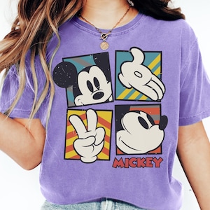 A person wearing a purple t-shirt with a graphic design featuring Mickey Mouse and the peace sign.