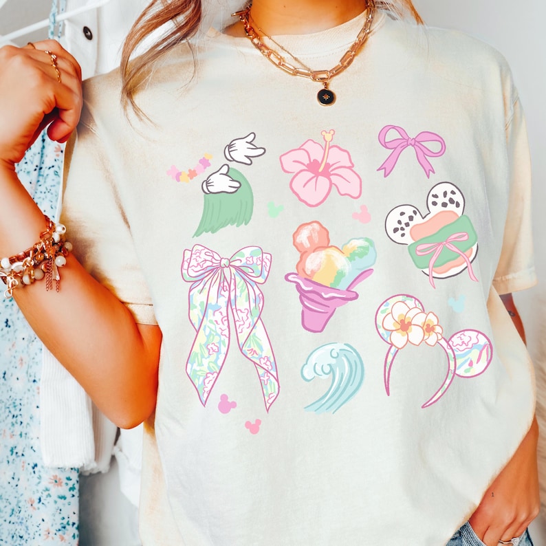 A person wearing a white t-shirt with various cartoon-style illustrations, including a bow, flowers, and other whimsical designs.