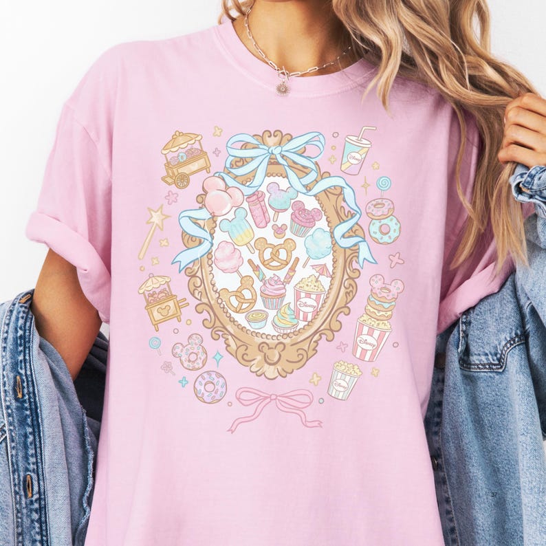 A woman wearing a pink t-shirt with a colorful graphic design featuring various cartoon-like objects and decorations.