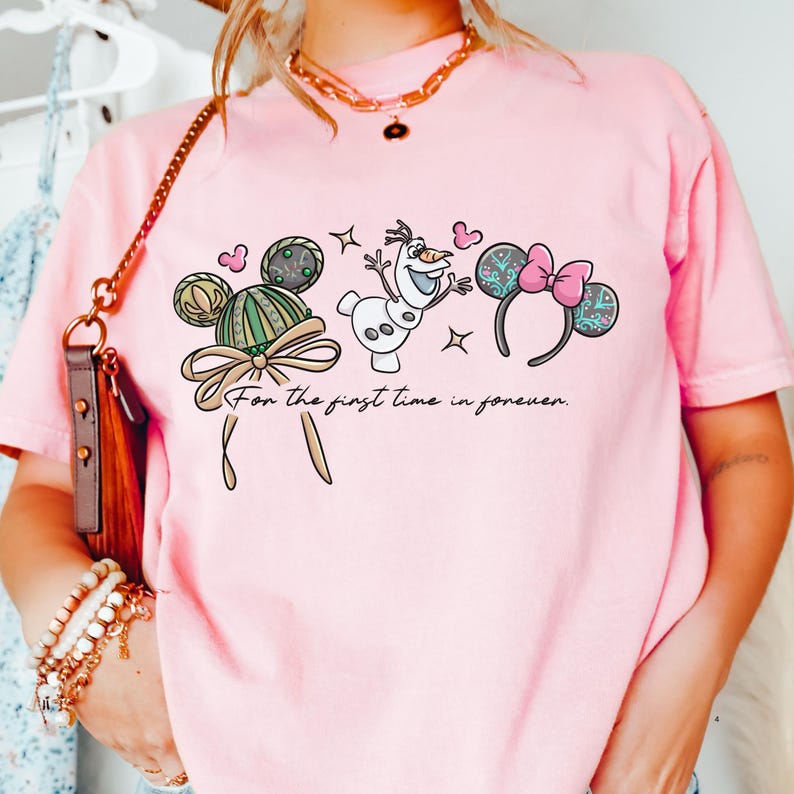 A person wearing a pink t-shirt with a graphic design featuring a character from the Disney movie Frozen, along with other Disney-themed elements.