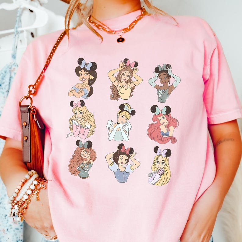 A person wearing a pink t-shirt with a graphic of various Disney princesses.