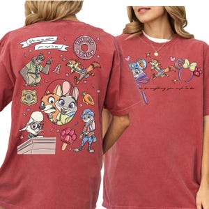a red t-shirt with a colorful graphic design of cartoon characters and various objects, including a police officer, a rabbit, and other whimsical elements.