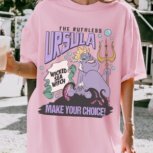 A person wearing a pink t-shirt with a graphic design featuring a character from the Disney animated film "The Little Mermaid".