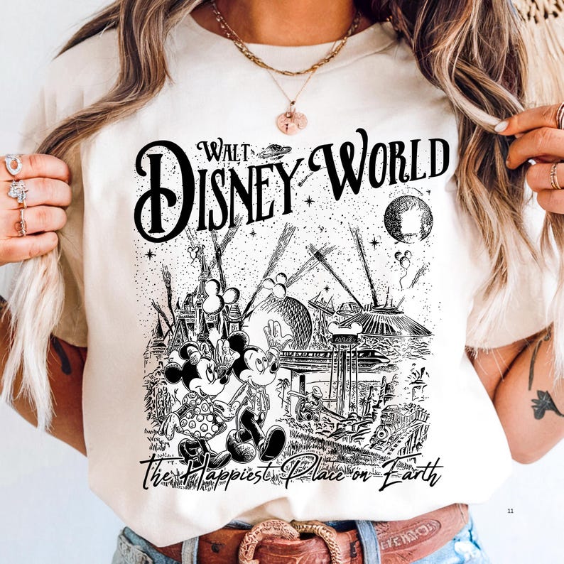 A person wearing a white t-shirt with a graphic design depicting Mickey Mouse and Minnie Mouse in a whimsical, fantastical landscape.